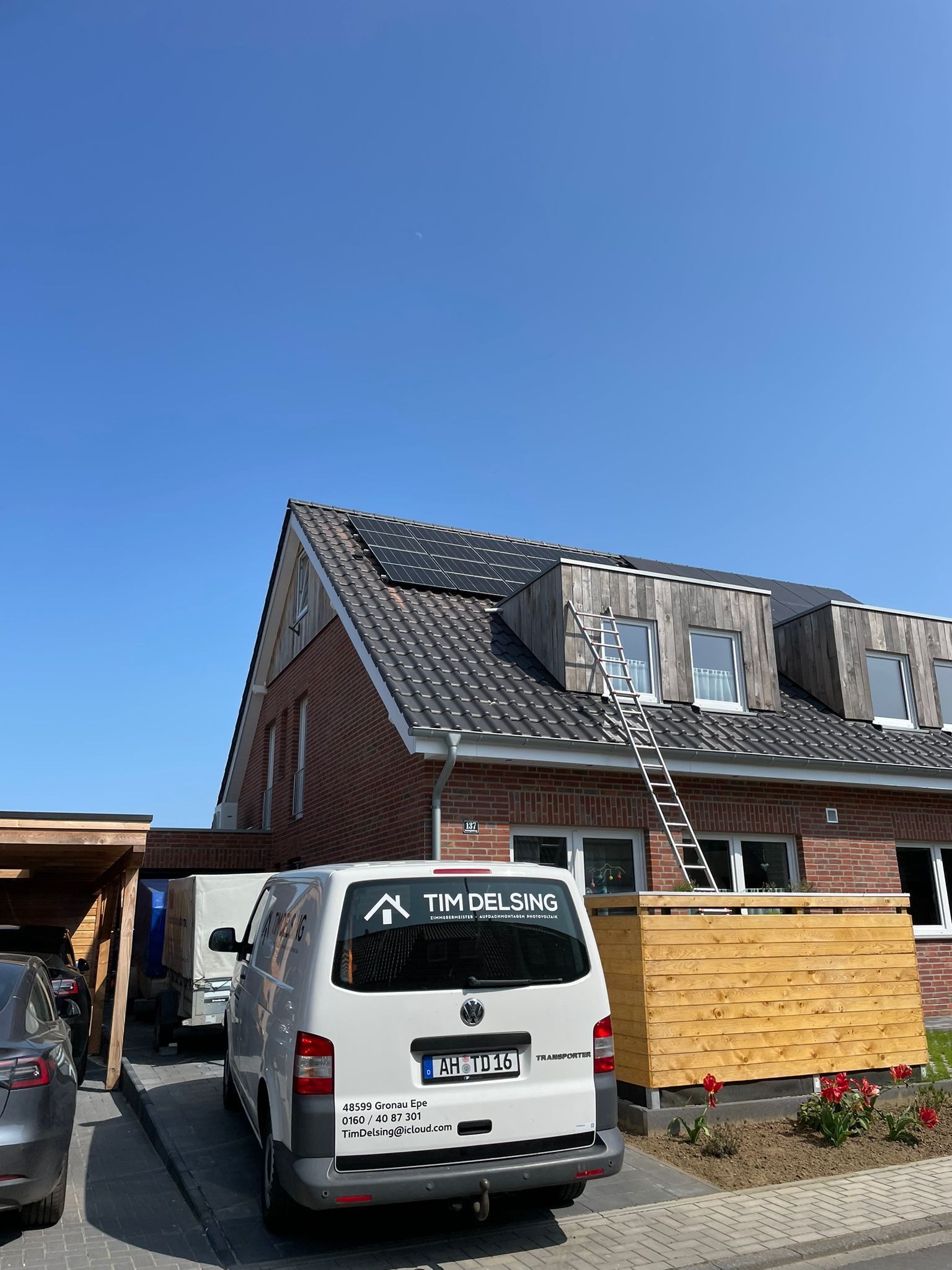 Ein weißer Lieferwagen parkt vor einem Haus mit Solarzellen auf dem Dach.