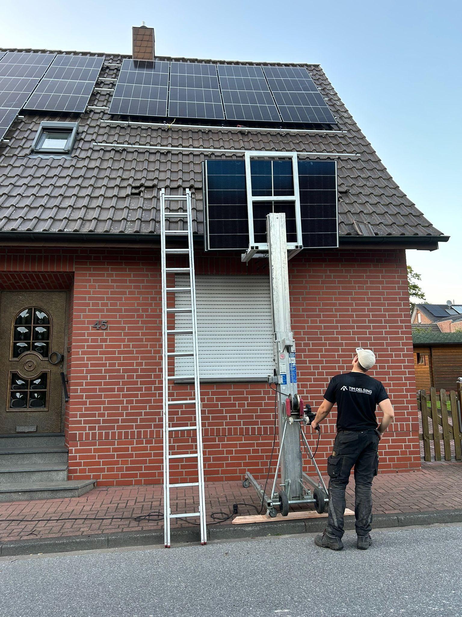 Ein Mann installiert Solarmodule auf dem Dach eines Backsteinhauses.