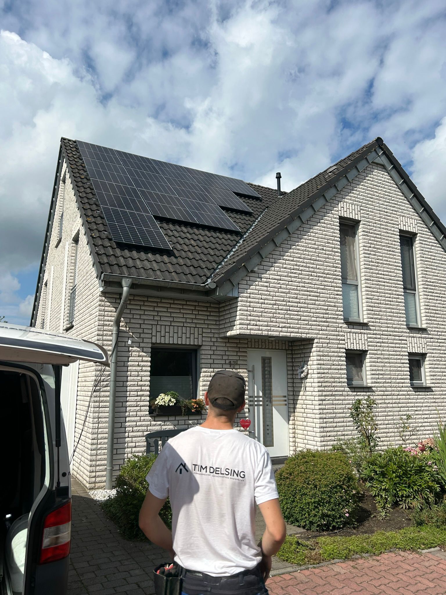 Ein Mann steht vor einem Haus mit Solarzellen auf dem Dach.
