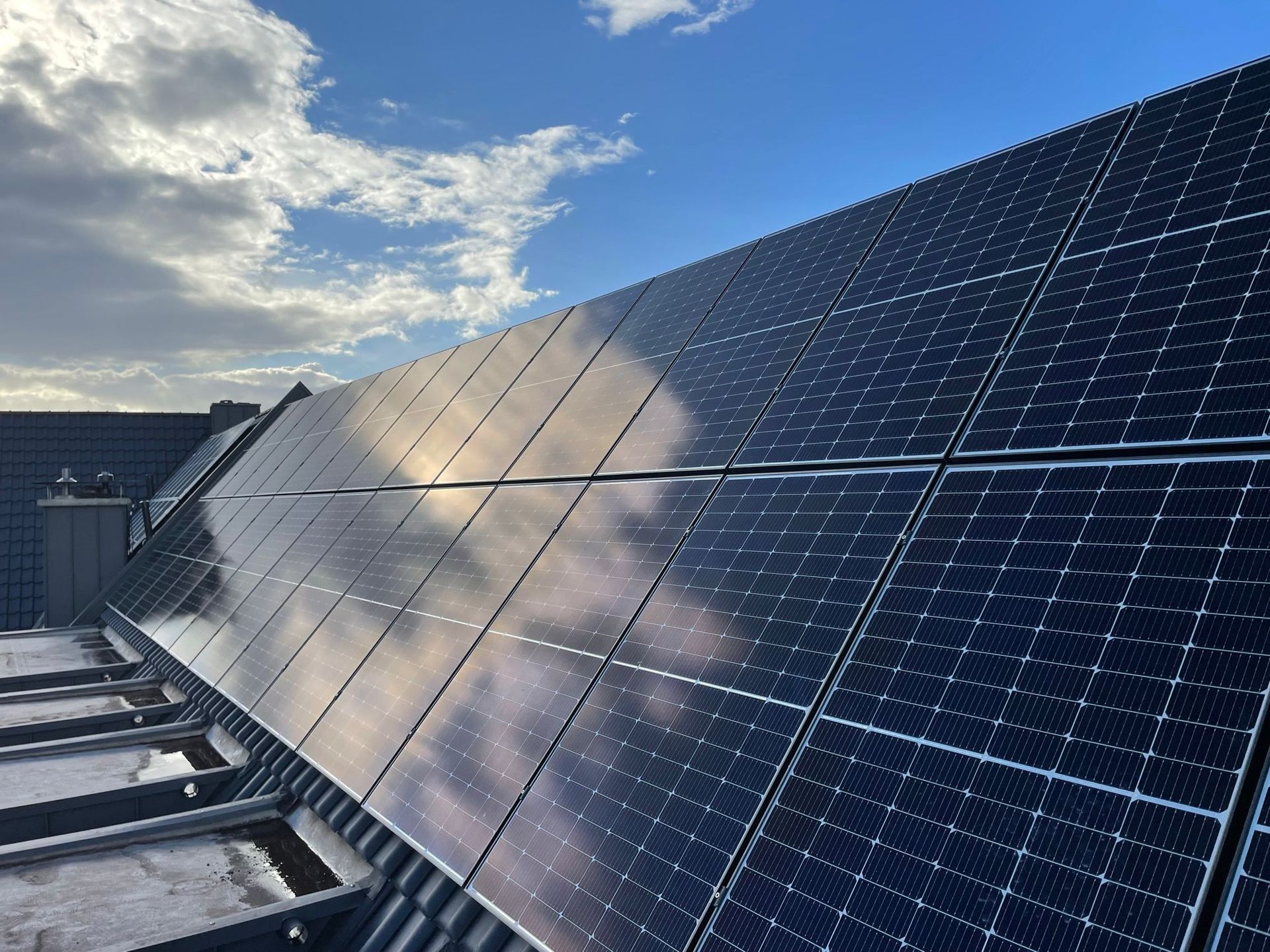 Eine Reihe von Solarmodulen auf einem Dach mit einem blauen Himmel im Hintergrund.