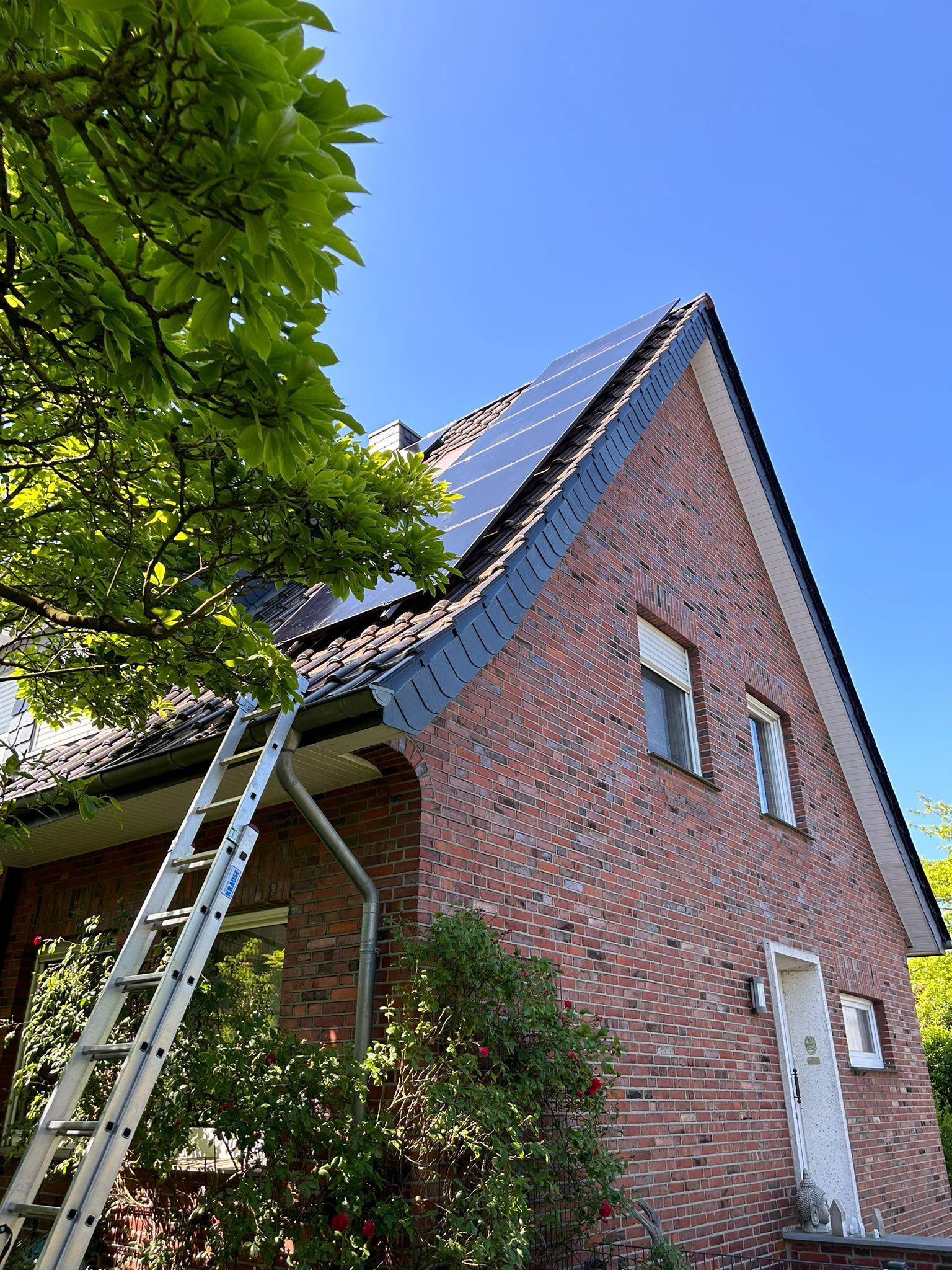 An der Seite eines Backsteinhauses mit Solarzellen auf dem Dach steht eine Leiter.