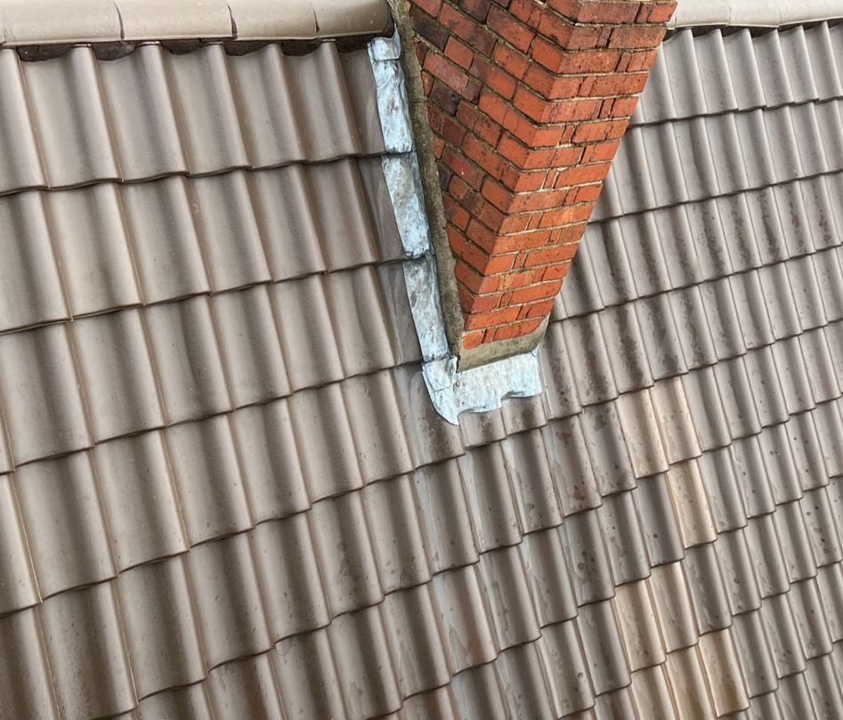 Auf einem Ziegeldach sitzt ein gemauerter Schornstein.