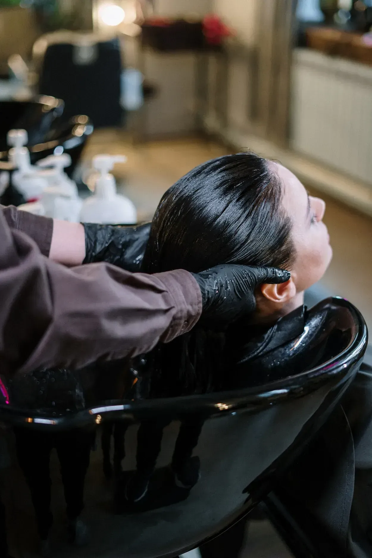 Una persona se lava el cabello en una peluquería. Un estilista con guantes le masajea suavemente el cuero cabelludo.