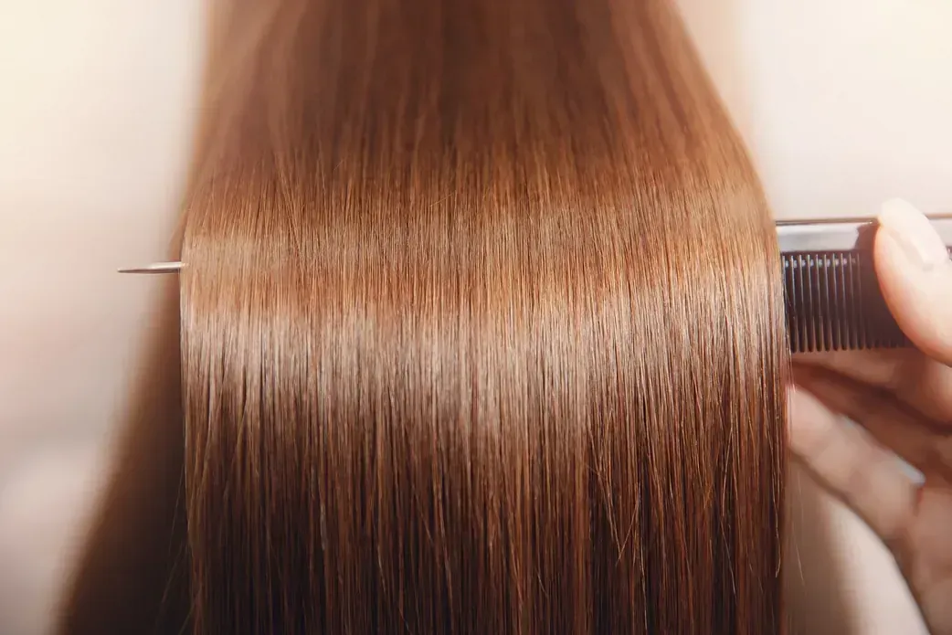 Peinando a mano cabello castaño largo y liso con un peine, resaltando su textura suave.