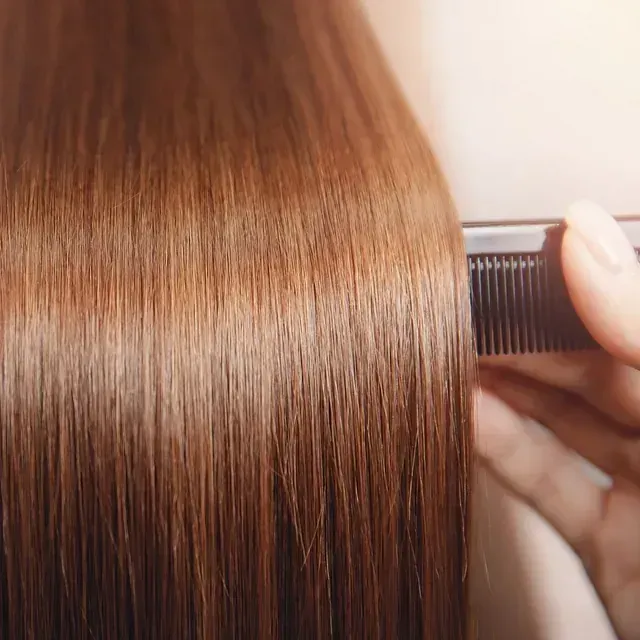 Una mano peina un cabello liso de color marrón rojizo, que está cerca de la cámara.