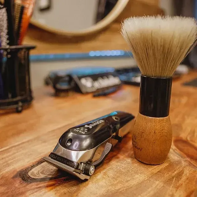 Primer plano de las herramientas de un barbero: una maquinilla y una brocha de afeitar, colocadas sobre un mostrador de madera, probablemente en una barbería.