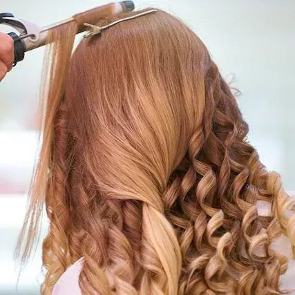 Persona que riza cabello largo, en capas y de color ombré con un rizador en un salón de belleza.