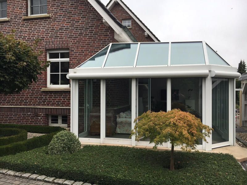 Ein Backsteinhaus mit einem weißen Wintergarten davor