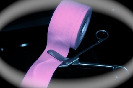 Un par de tijeras cortando un rollo de cinta rosa