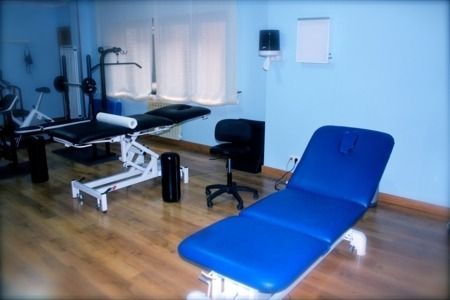 Una mesa de masaje azul está en una habitación con otras mesas.