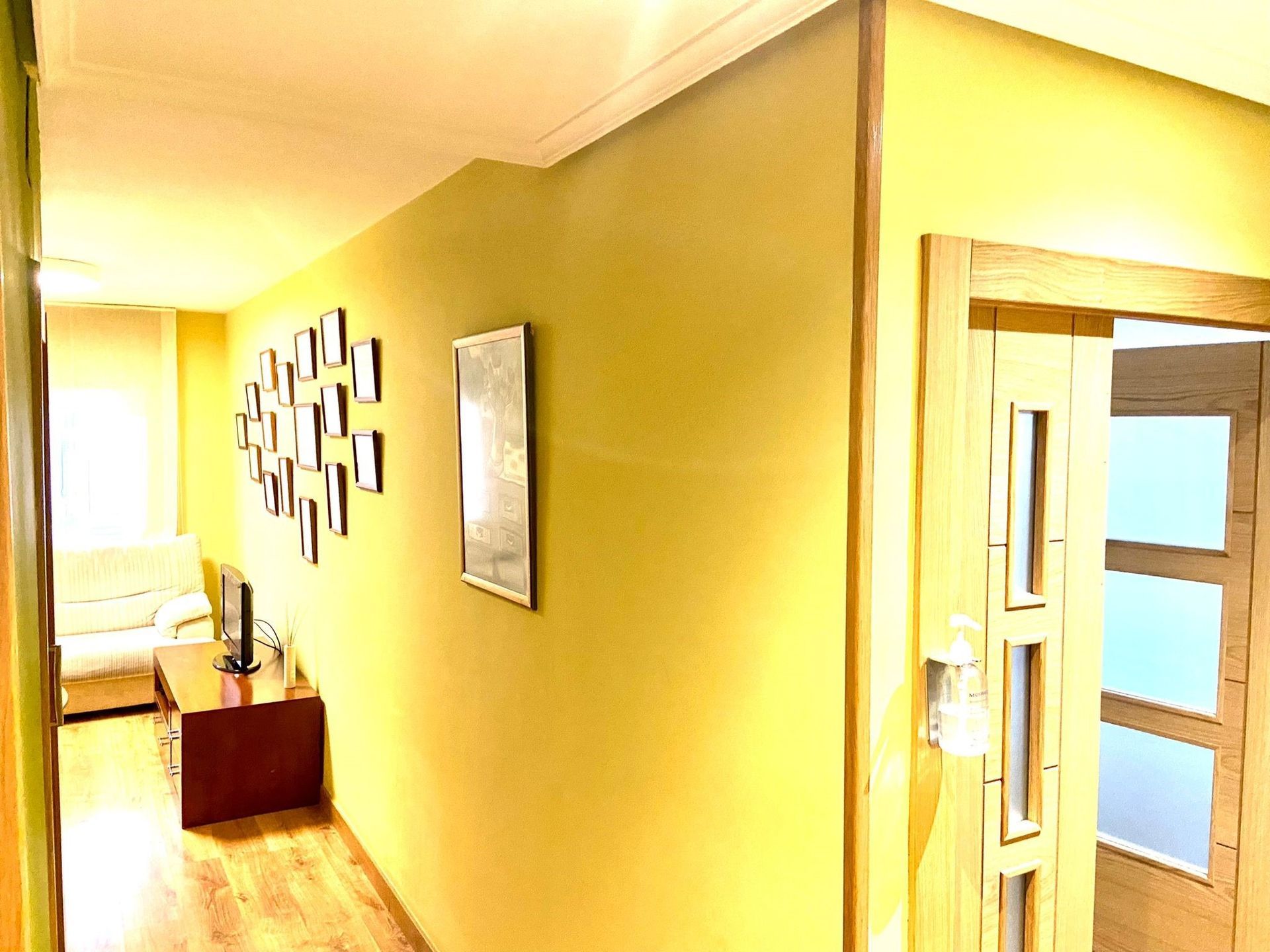 Un pasillo con paredes amarillas y suelos de madera que conduce a una sala de estar.