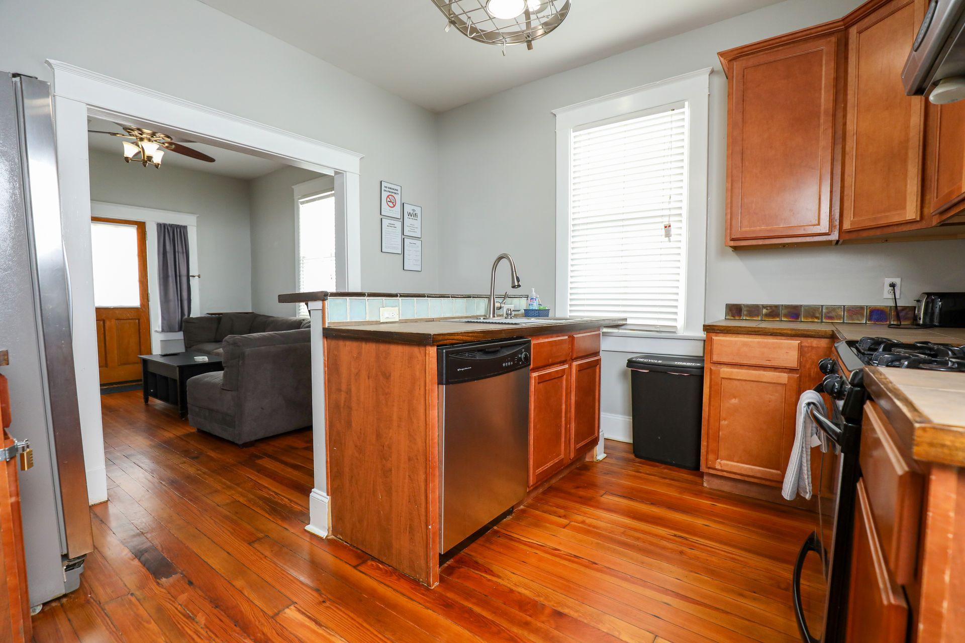 Long, narrow kitchen/dining room. Dark table with wooden chairs, leading to a sitting area. Green, white, and pink walls.