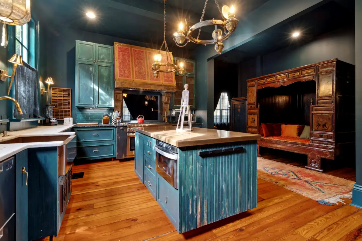 Dark kitchen with teal cabinets, wooden floor, ornate wood canopy bed and island.