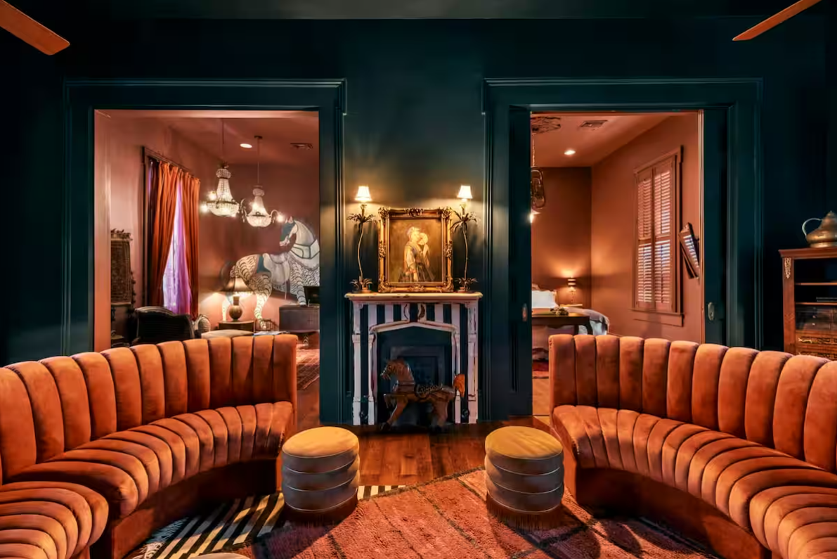 A luxurious living room with two orange curved sofas facing a fireplace, with rooms visible on each side.