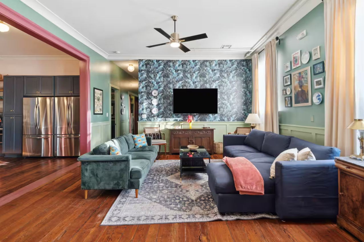 A living room with teal walls, a blue sectional sofa, and a patterned wallpaper wall.