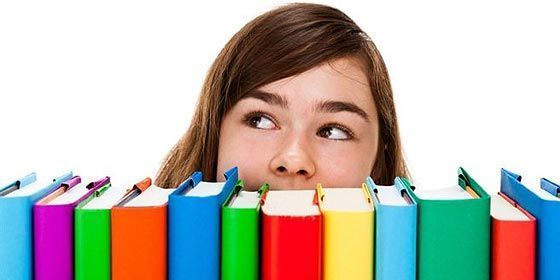 Una niña mira fijamente una pila de libros coloridos.