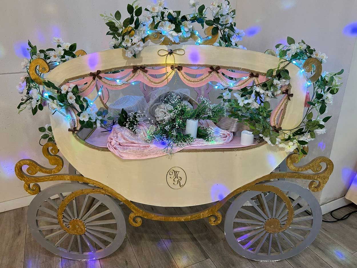 Un carruaje de madera decorado con flores y luces está sentado sobre un piso de madera.