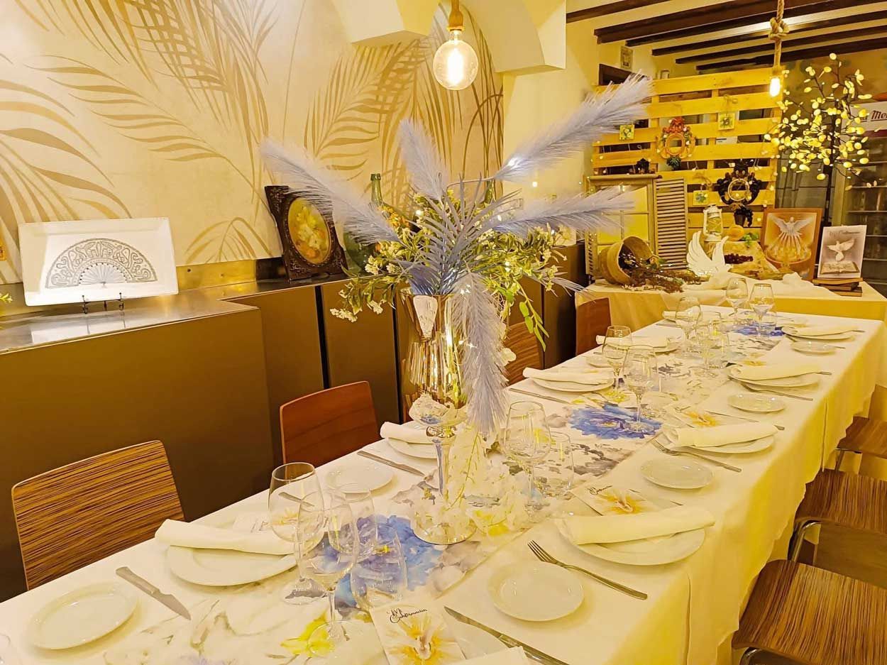 Una mesa larga con platos, cubiertos y un jarrón con flores encima.