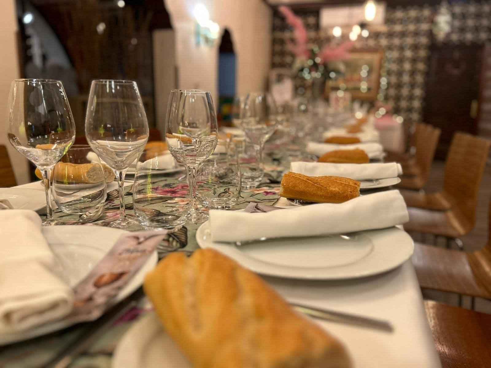Una mesa larga con platos, servilletas, pan y copas de vino.