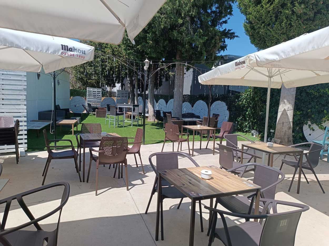 Un patio con mesas, sillas y sombrillas en un día soleado.