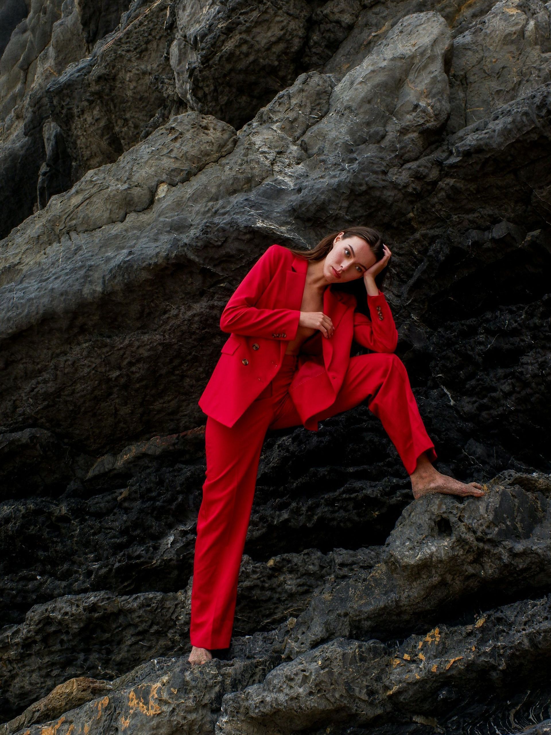 Una mujer con un traje rojo está sentada en una roca.
