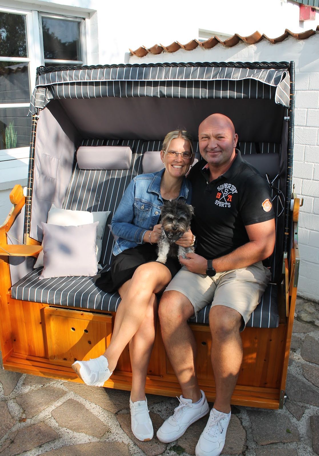 Ein Mann und eine Frau sitzen mit einem Hund auf einem Strandstuhl.