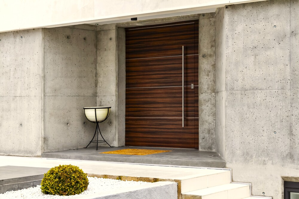 Una puerta de madera con manija de acero inoxidable se encuentra frente a una pared de hormigón.