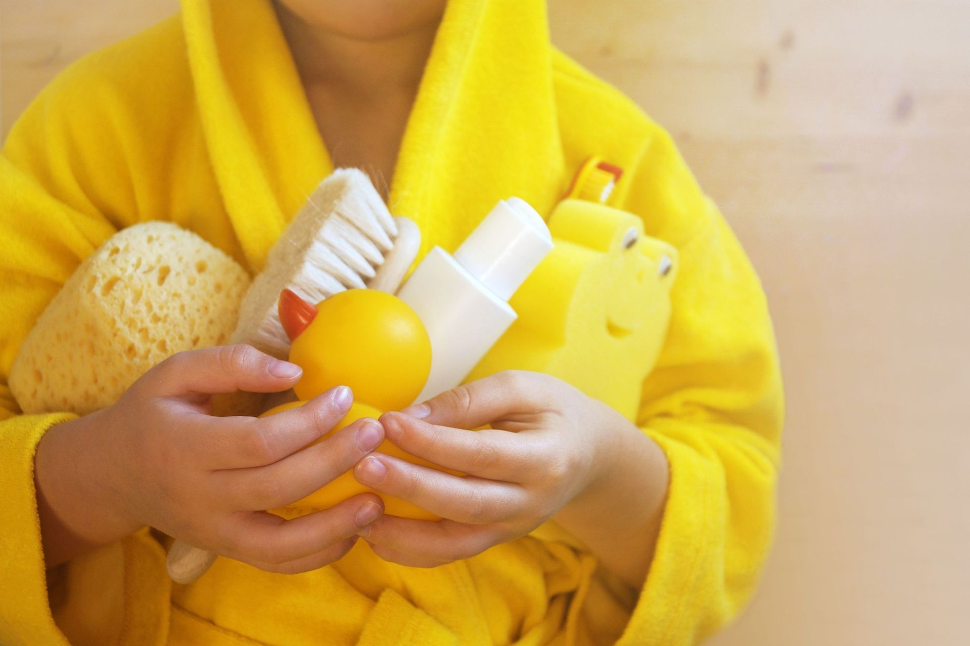 Niño con bata amarilla sosteniendo juguetes de baño y artículos de tocador.