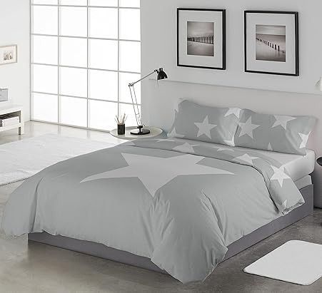 Ropa de cama con estampado de estrellas en tonos grises y blancos sobre una cama en un dormitorio moderno y minimalista.