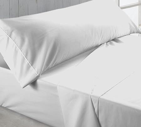 Sábanas blancas y almohadas sobre una cama, iluminada por una luz suave.