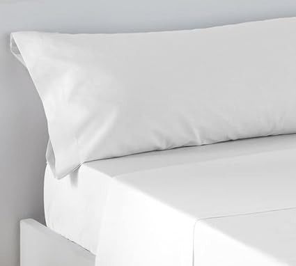 Almohada blanca sobre un juego de sábanas blancas, entorno de dormitorio minimalista.