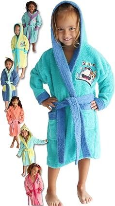 Chica en bata azul con capucha, sonriendo, túnicas de varios colores detrás de ella.