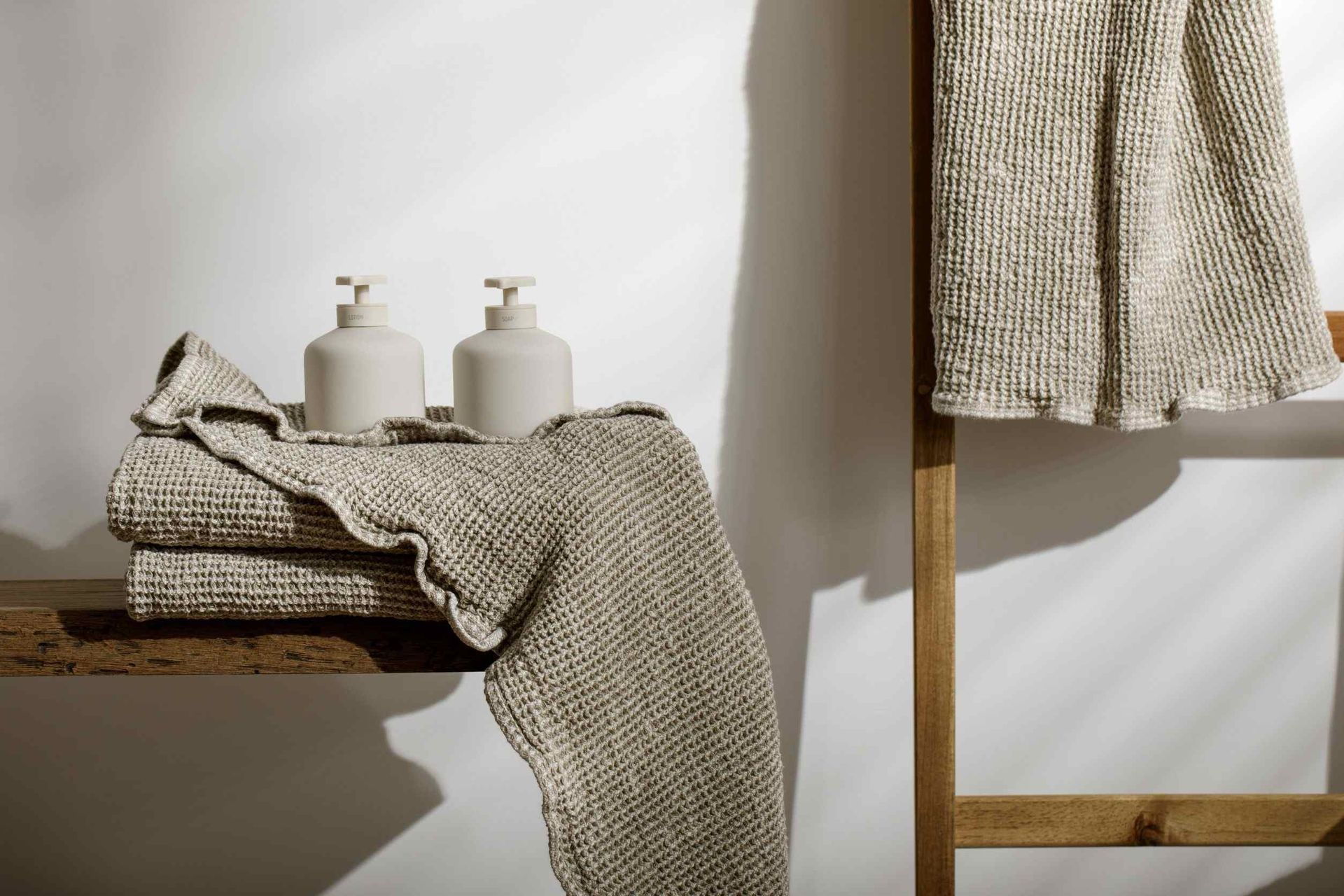 Dos dispensadores de jabón beige y toallas en un estante de madera, otra toalla colgada en una escalera.