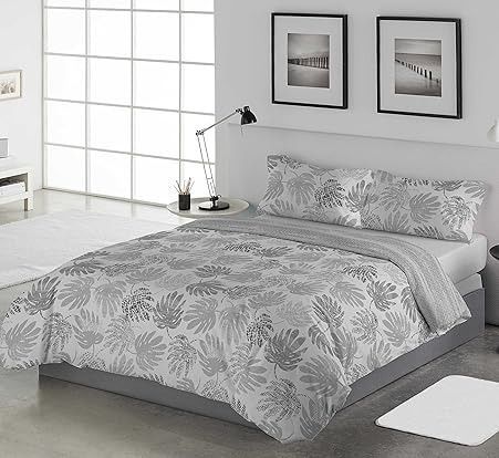 Juego de cama con motivos florales de color gris sobre una cama en un dormitorio con obras de arte, una lámpara y una ventana.