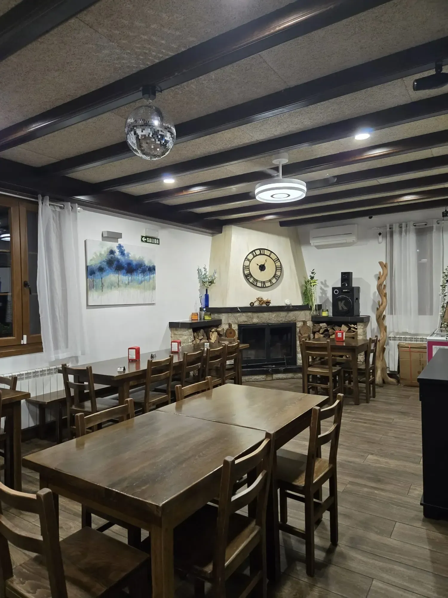 Interior de restaurante con mesas y sillas, una chimenea y una bola de discoteca colgando del techo.