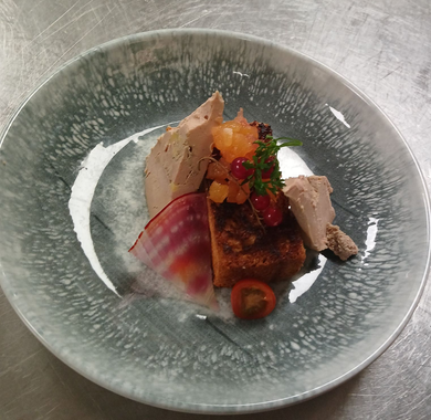 Plat gastronomique composé de poisson en tranches, de baies, d'herbes et de sauce, présenté dans un bol gris.
