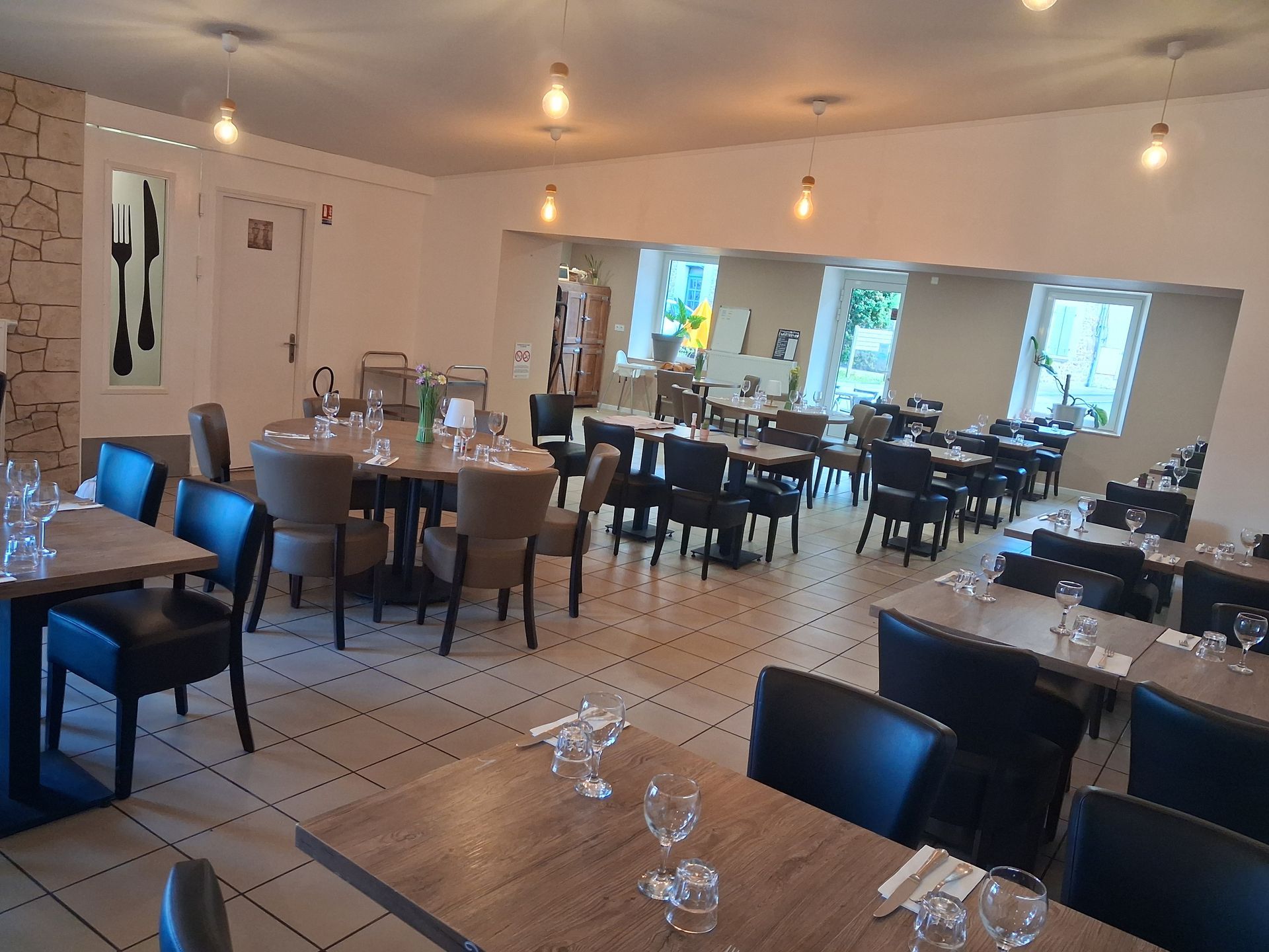Salle à manger de restaurant vide avec tables, chaises noires, suspensions lumineuses et lumière naturelle provenant des fenêtres