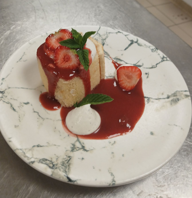 Dessert garni de fraises, nappé de sauce rouge et de menthe, présenté sur une assiette blanche à motif marbré.
