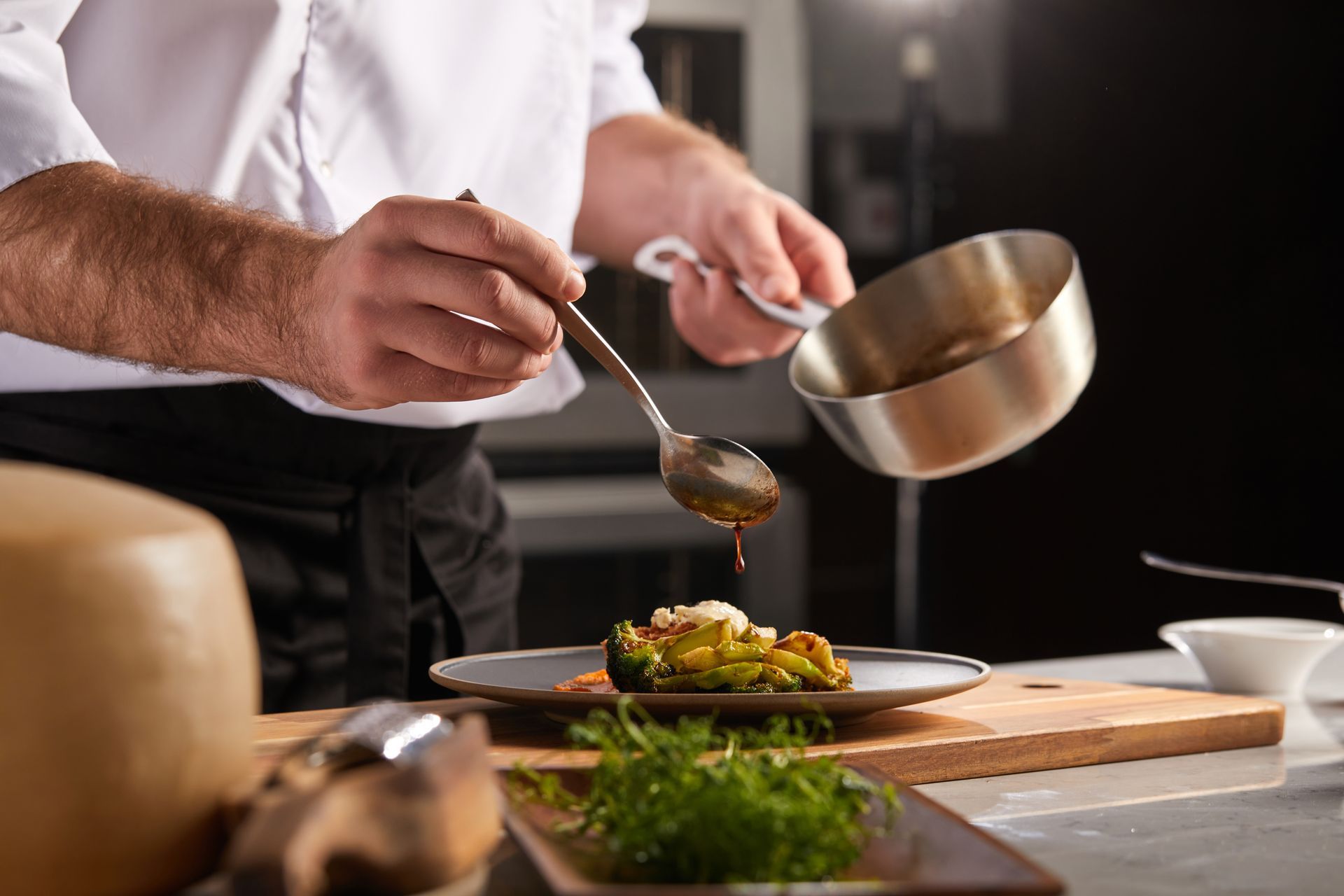 Un chef dresse un plat gastronomique, versant de la sauce d'une casserole dans une cuisine