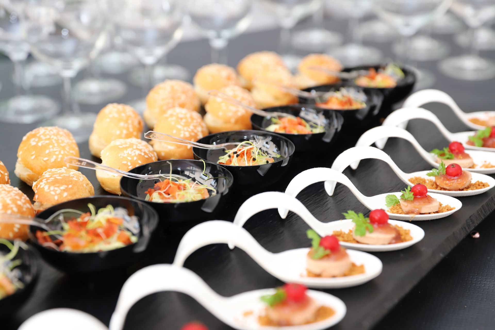 Élégantes rangées de bouchées apéritives présentées sur des cuillères et des bols de service noirs, dans un buffet.