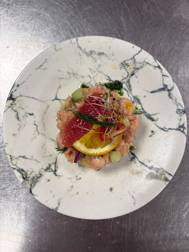 Assiette de fruits de mer gastronomique avec tranches de citron et herbes, présentée sur une assiette en marbre blanc.