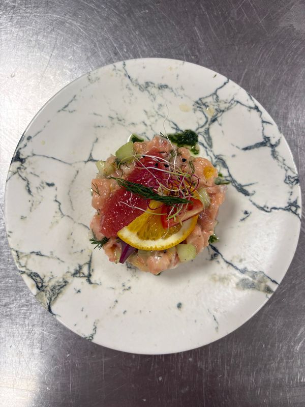 Assiette de fruits de mer gastronomique avec tranches de citron et herbes, présentée sur une assiette en marbre blanc.