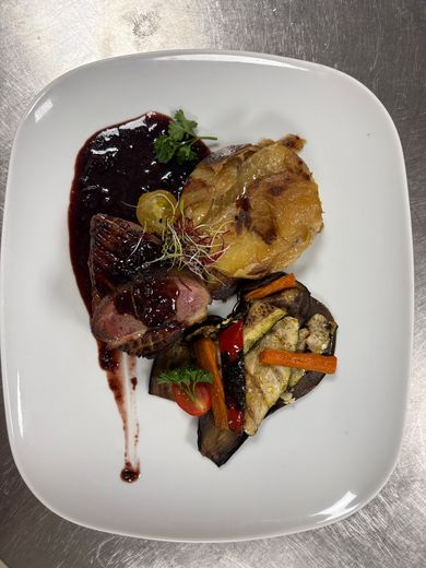 Plat gastronomique présenté dans une assiette carrée blanche, composé d'une sauce brune, de viande saisie, de légumes et de pommes de terre croustillantes.