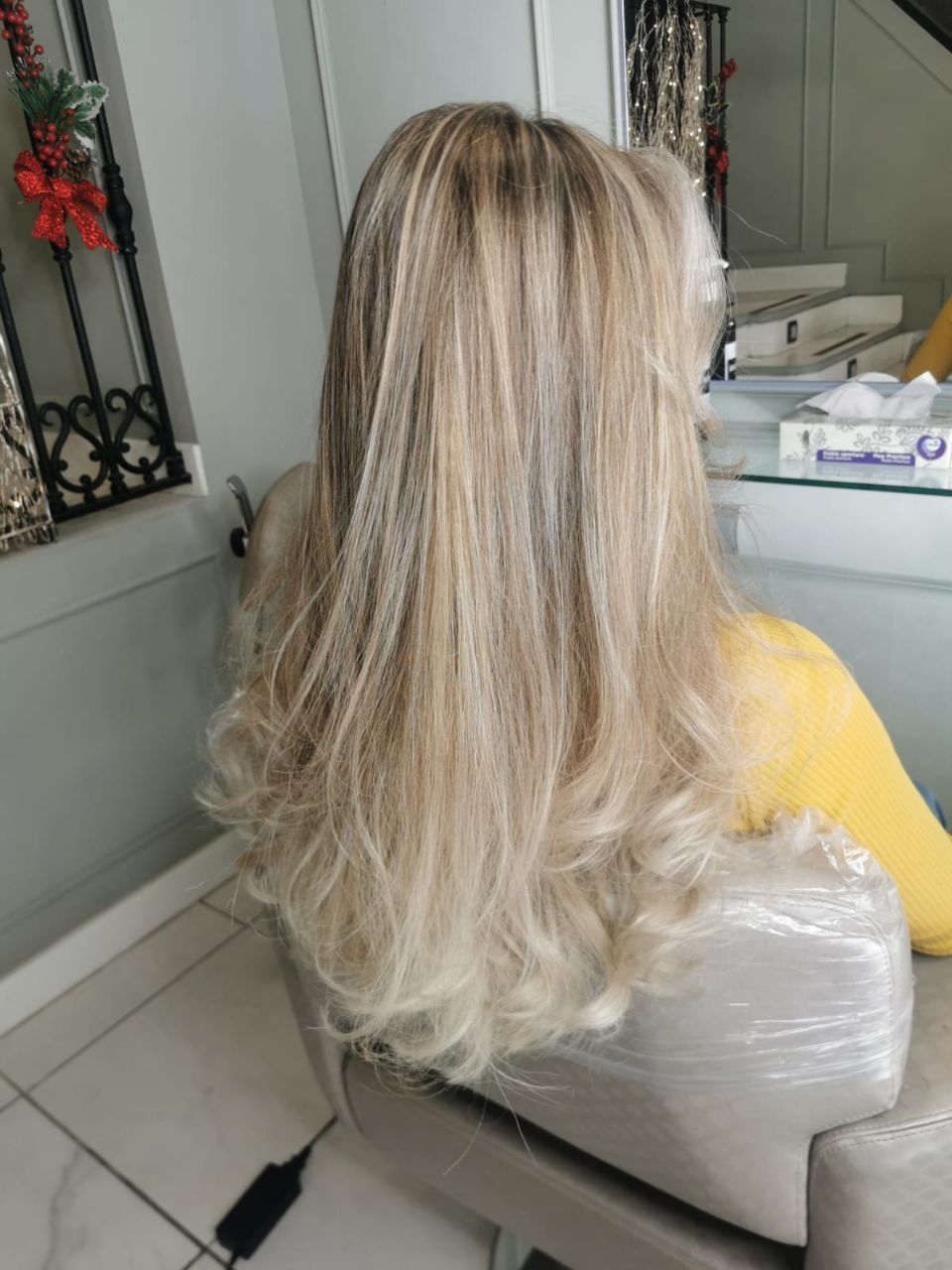 Cabello rubio peinado en ondas sueltas, visto desde atrás en una silla de peluquería con una capa amarilla.