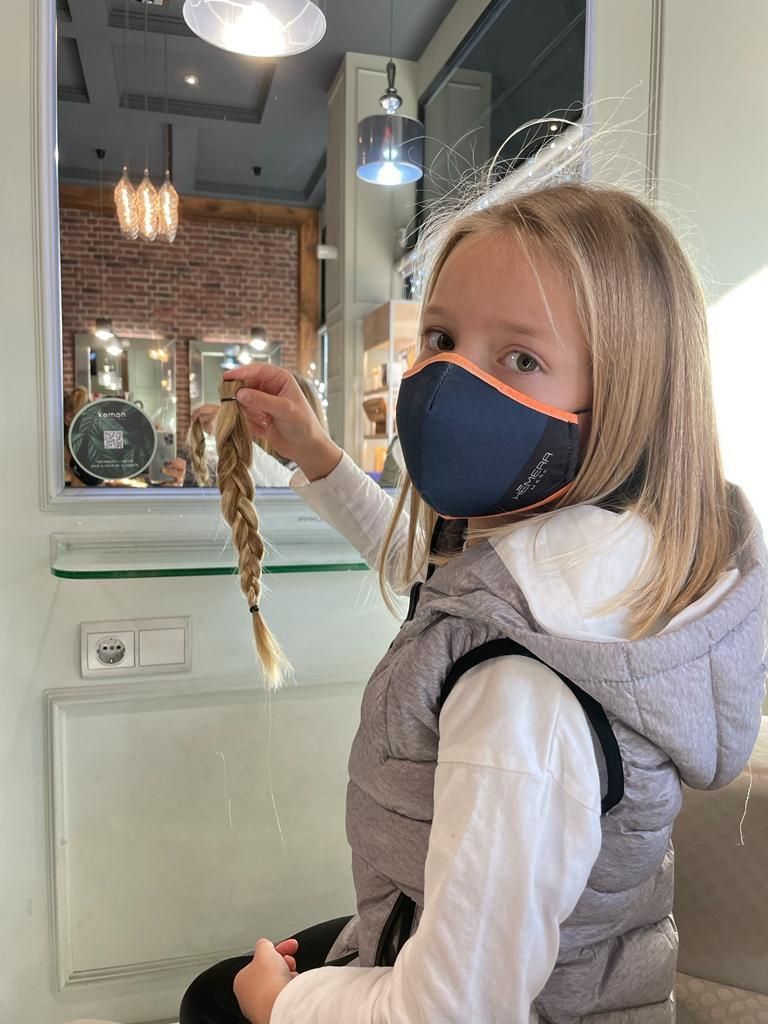 Niño con mascarilla sosteniendo un bocadillo alargado dentro de una cafetería o panadería.