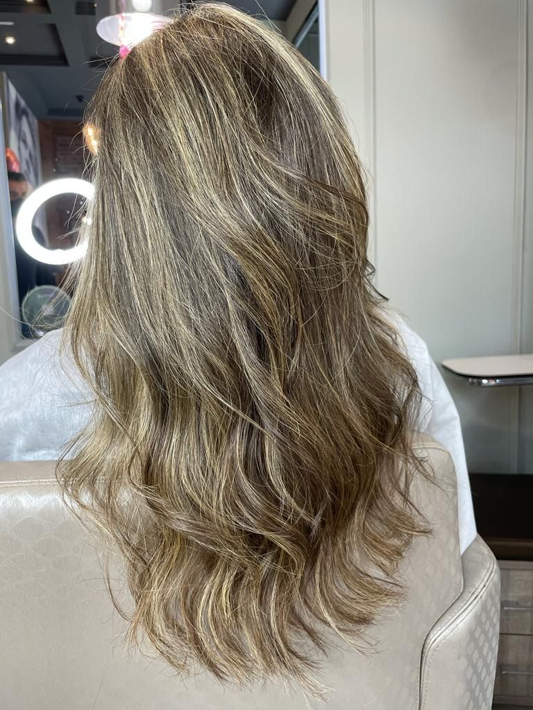 Cabello rubio largo y ondulado con reflejos sutiles, visto desde atrás en una silla de peluquería.