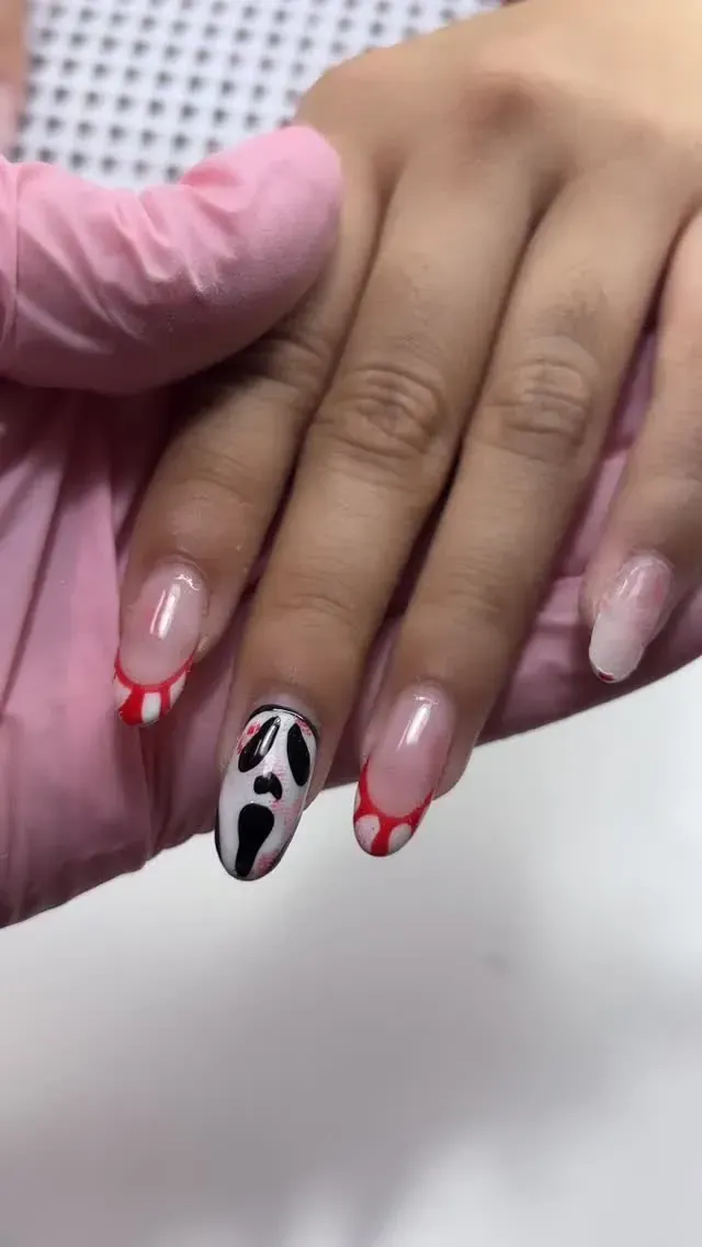 Mano con diseño de uñas que presenta una máscara de Scream y uñas con puntas rojas.