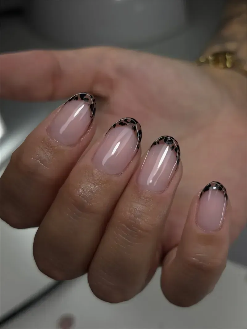 Primer plano de una mano con uñas de forma ovalada con una manicura francesa con diseño de estampado de leopardo.