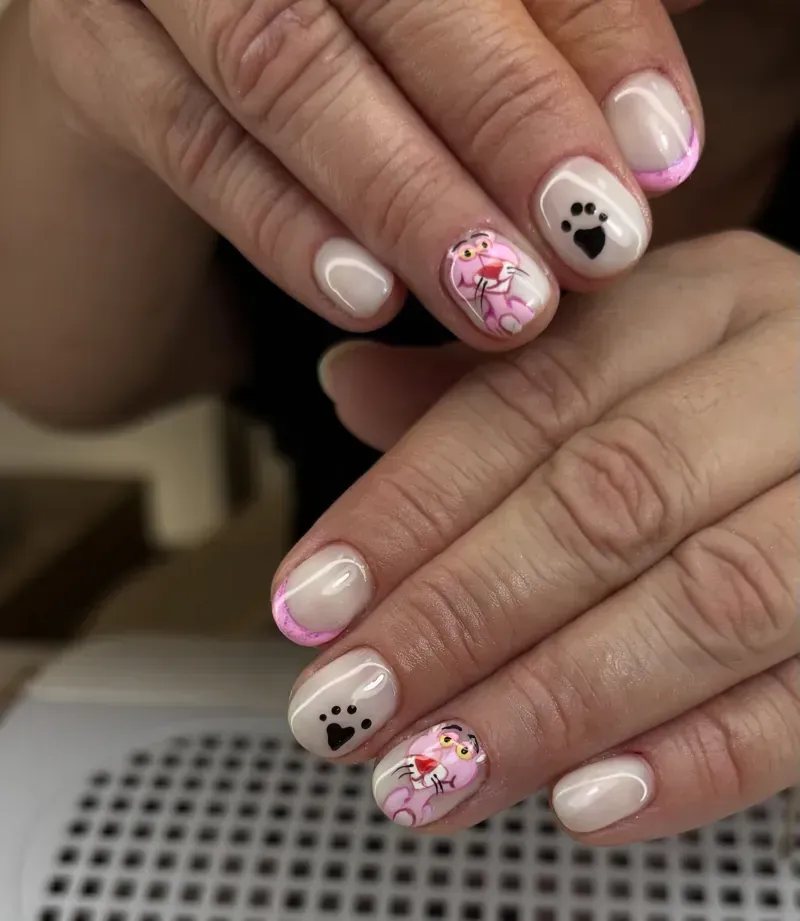 Manos con uñas de color beige, con líneas de acento rosas, Pantera Rosa y huellas de patas.