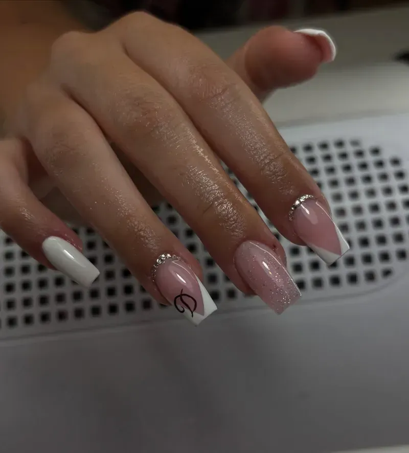 Mano con uñas largas y cuadradas; puntas francesas blancas y rosas, algunas adornadas con pequeños cristales.